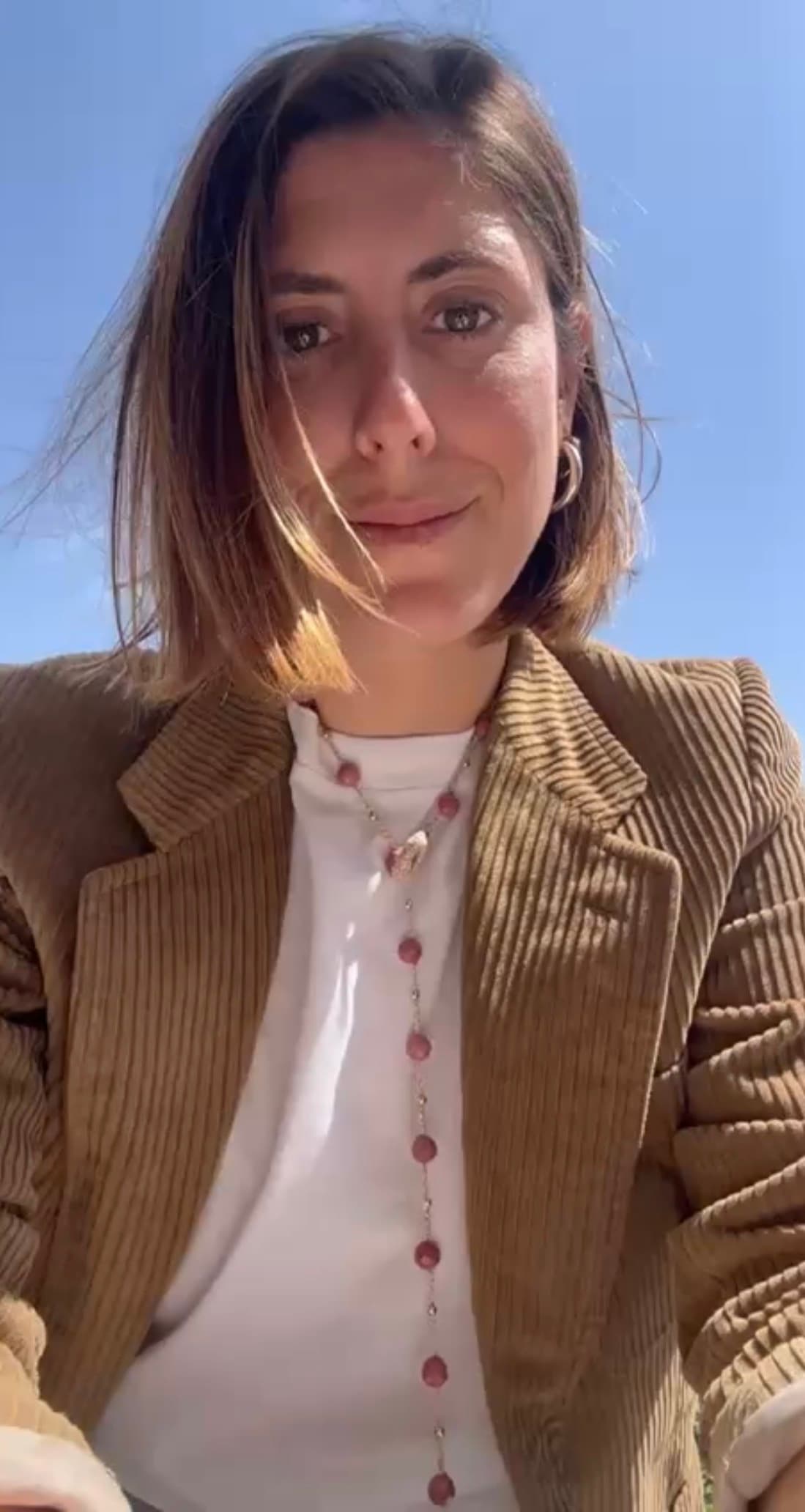 Donna con capelli castani corti, blazer di velluto marrone e collana con perline rosa.
